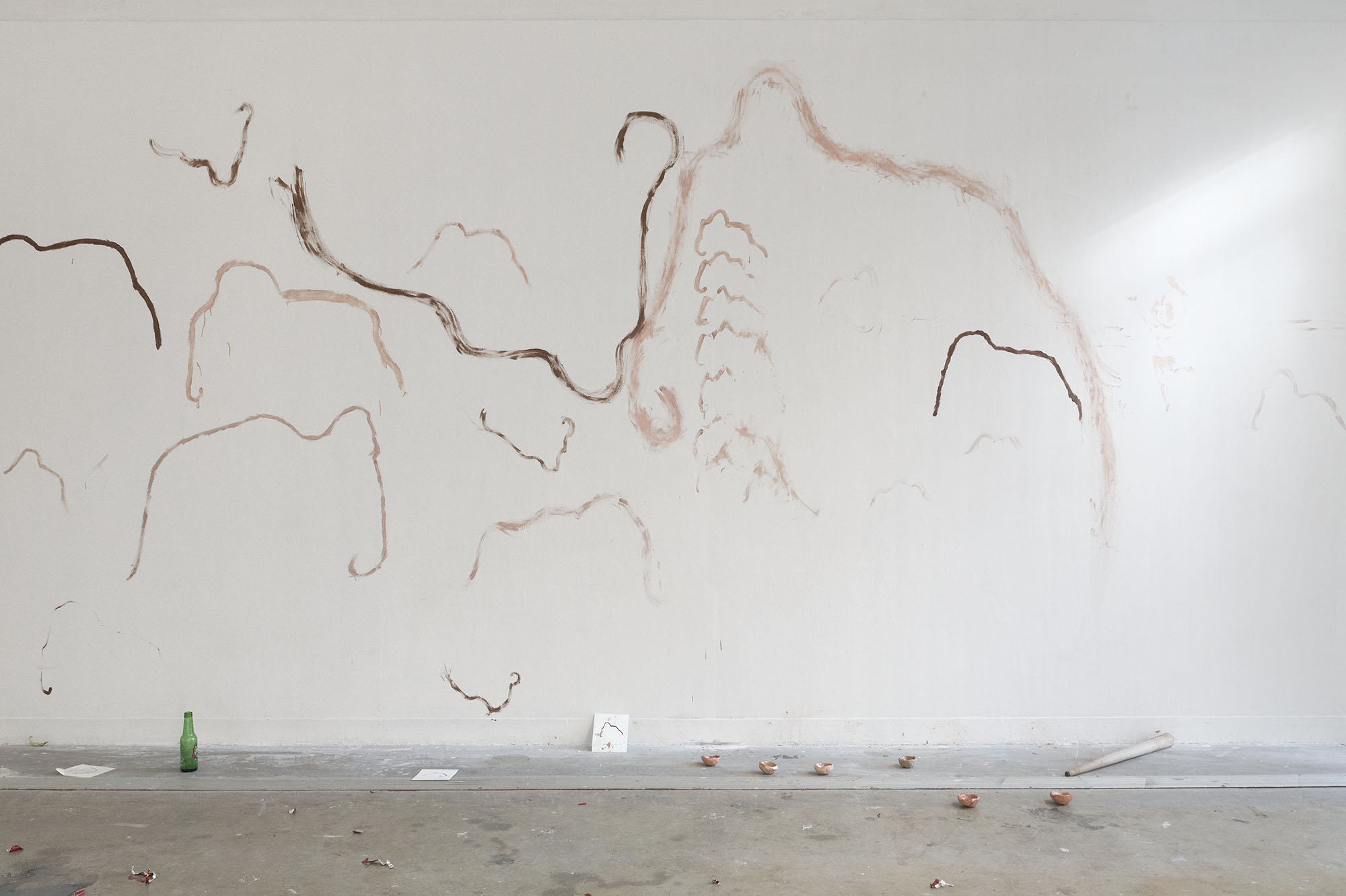 photo du lendemain : un mur est recuvert de dessins de mammouth, des pots de peinture traine au sol à côté d'une bouteille de bière.